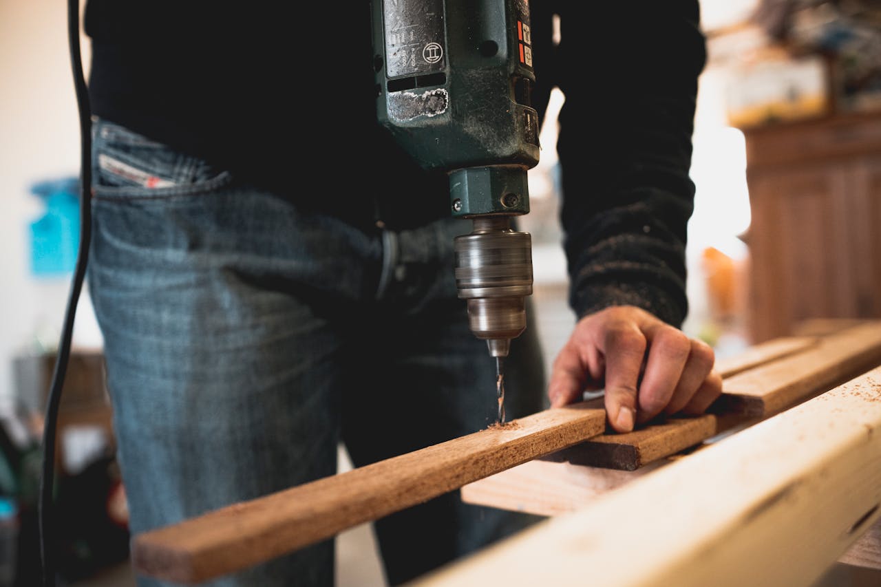 Close-up of a person using an electric drill on a wooden plank, showcasing detailed woodworking skills.